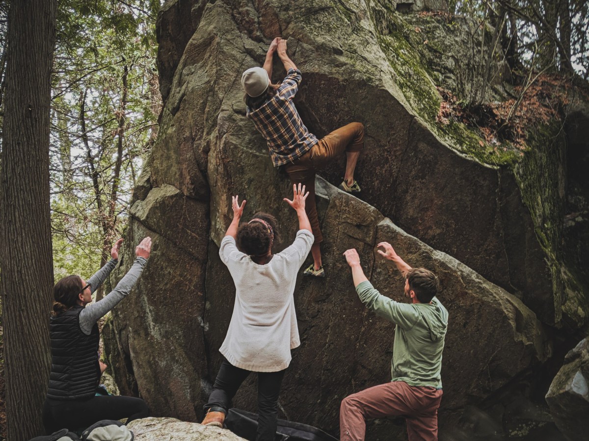 People supporting someone climbing a boulder